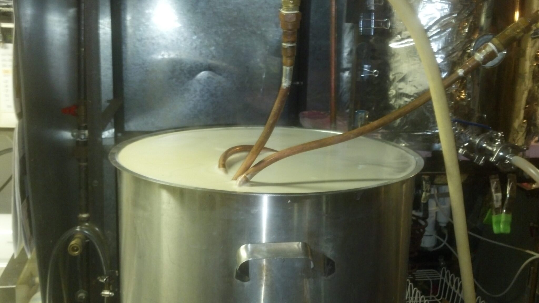 A large stainless pot full to the brim with beer wort. A copper submersible coil chiller pokes out at the top.
