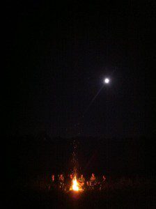 WIretreat062012 A group of friends sits around a campfire at night on a friend's farm in Wisconsin. A full moon is visible overhead.