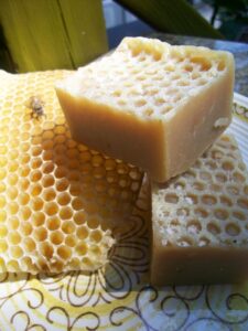Two bars of homemade beeswax soap from Alewyfe Apothecary with a piece of empty honeycomb on a yellow and brown midcentury modern ceramic transferware plate.. The soap bars are stamped with a honeycomb pattern.