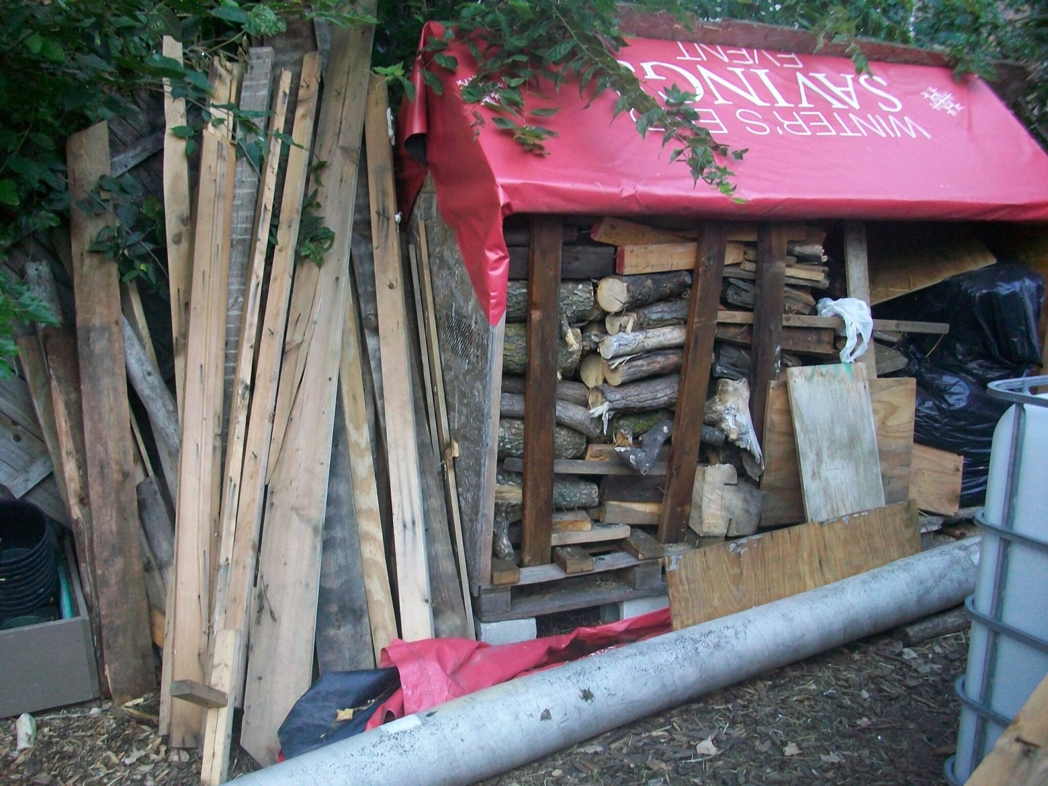An overflowing backyard woodshed made out of a shipping crate and old vinyl billboard tarps
