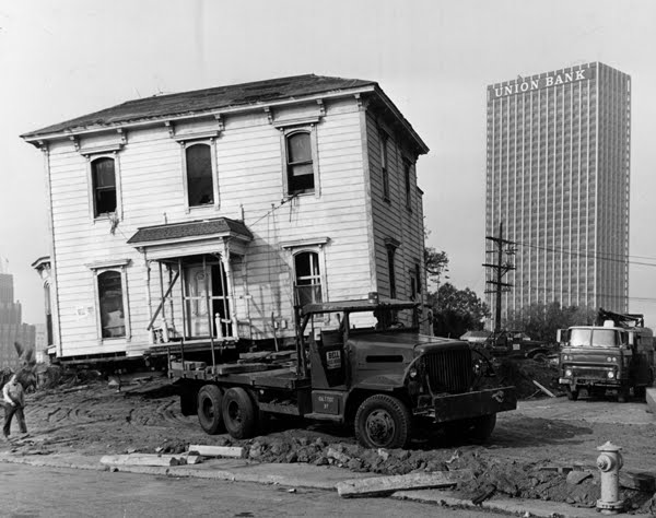 vintage black and white photo of a house being moved on skids pulled by a truck