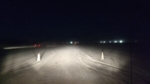 headlights illuminate road markers in the dark while driving into Black Rock City in the desert.