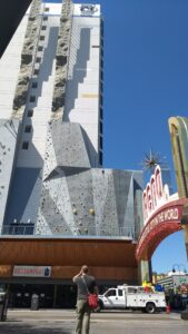The Reno archway sign over a street, with a tall rock climbing wall on the outside of our hotel behind it.