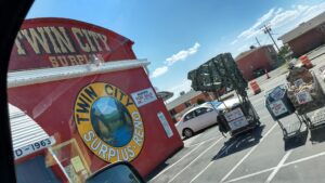 a large red building with a painted mural sign reading, "twin city surplus reno" in a parking lot. Carts filled with merchandise and hand painted signs are in some of the parking spots.