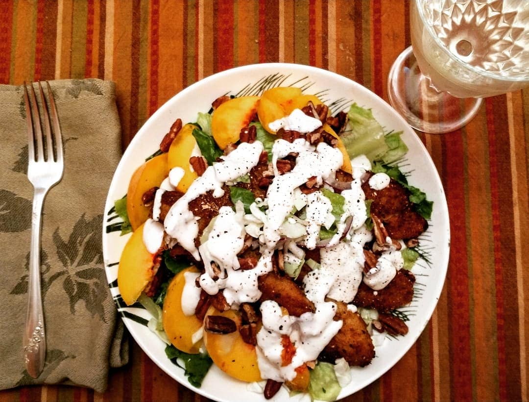 a place setting with a bowl salad greens, topped with southern fried catfish filets, fresh peach slices, pecans, and buttermilk ranch dressing