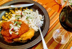 a plate with a venison chile relleno topped with smoky tomato roja sauce, with cilantro rice and a glass of red wine.