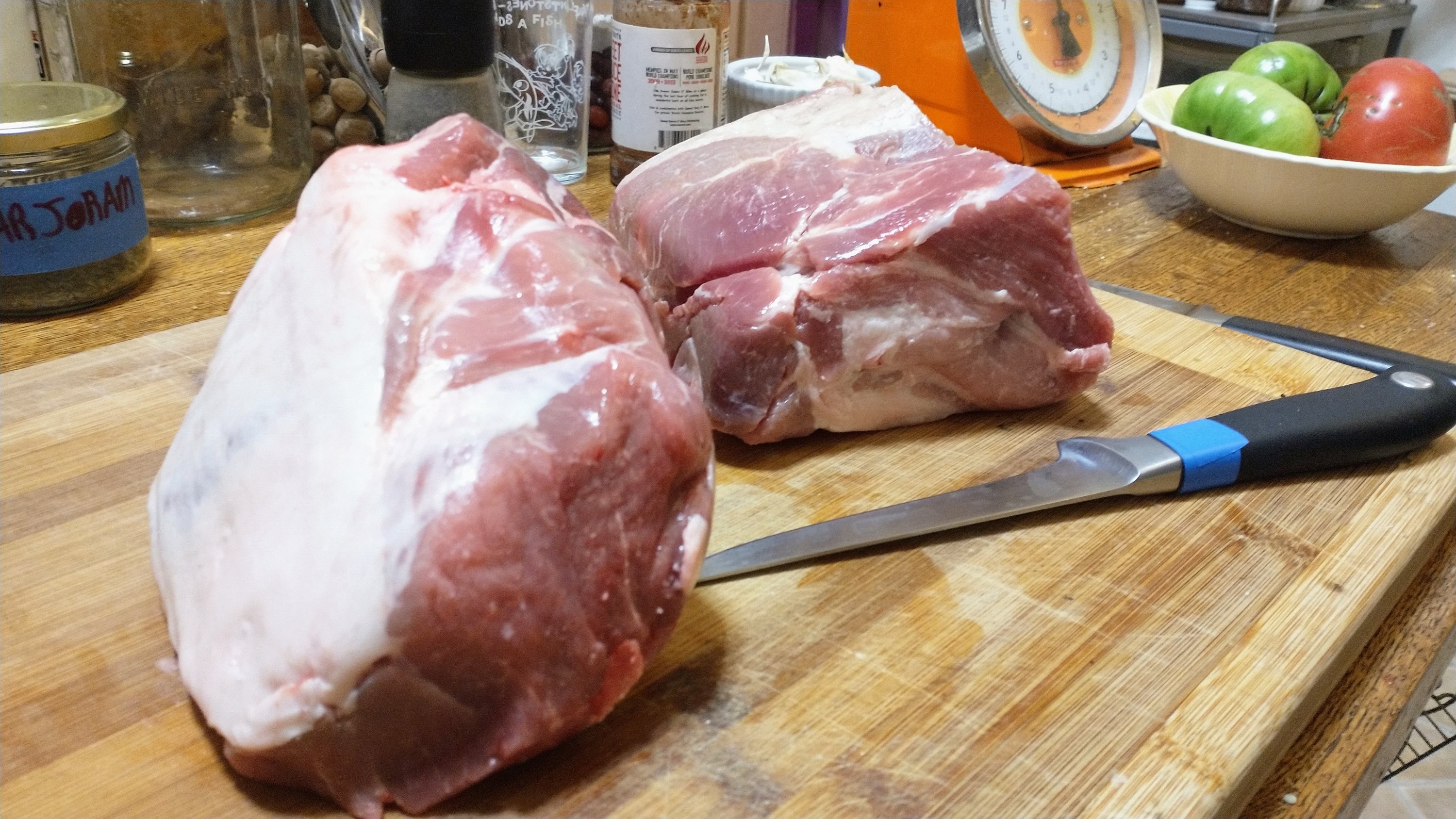 pork shoulder and a boning knife on a wooden cutting board.