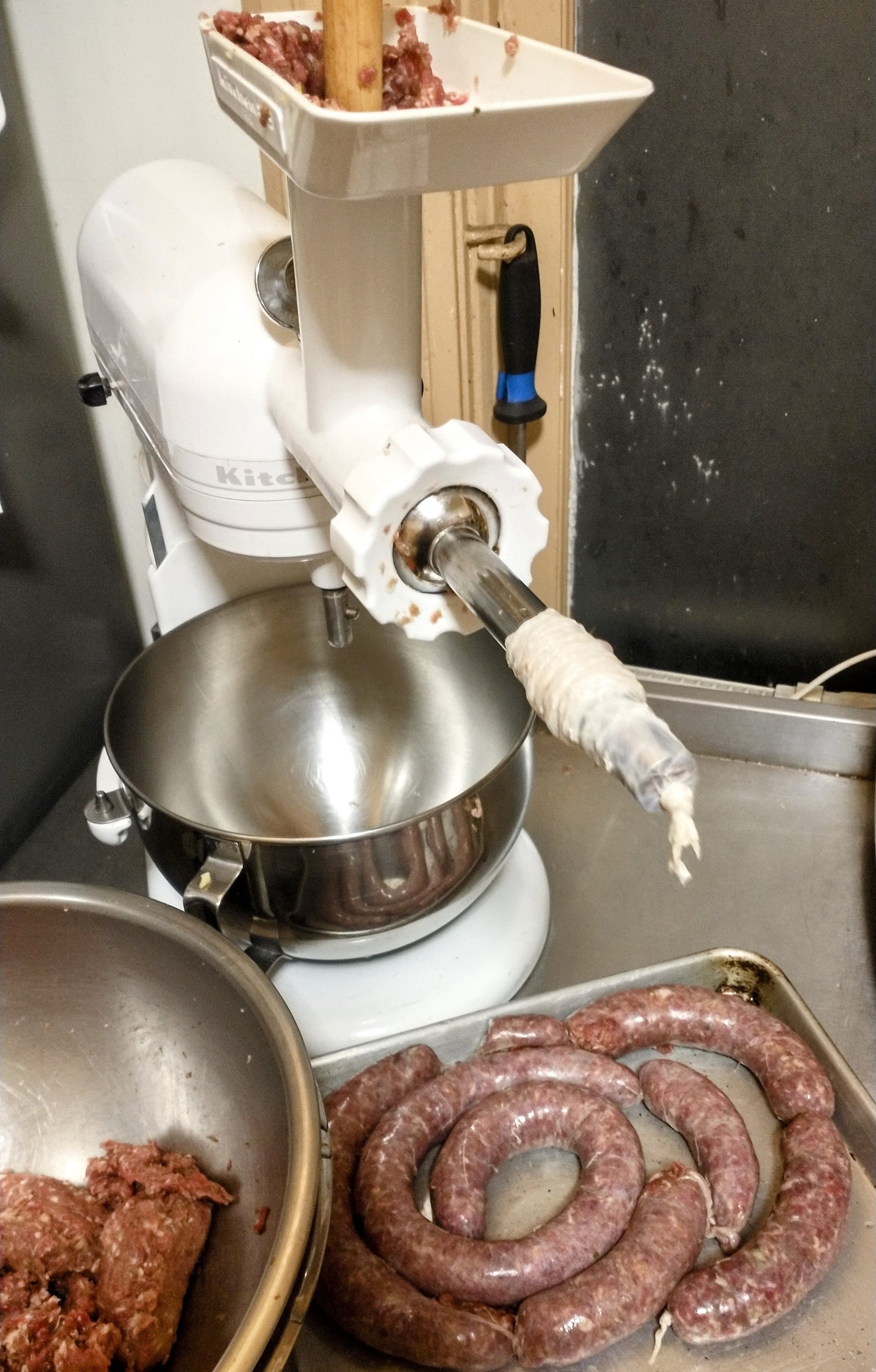 a kitchenaid stand mixer with a meat grinder and sausage stuffing attachment, filling sausage casings with venison wiejeska mixture.