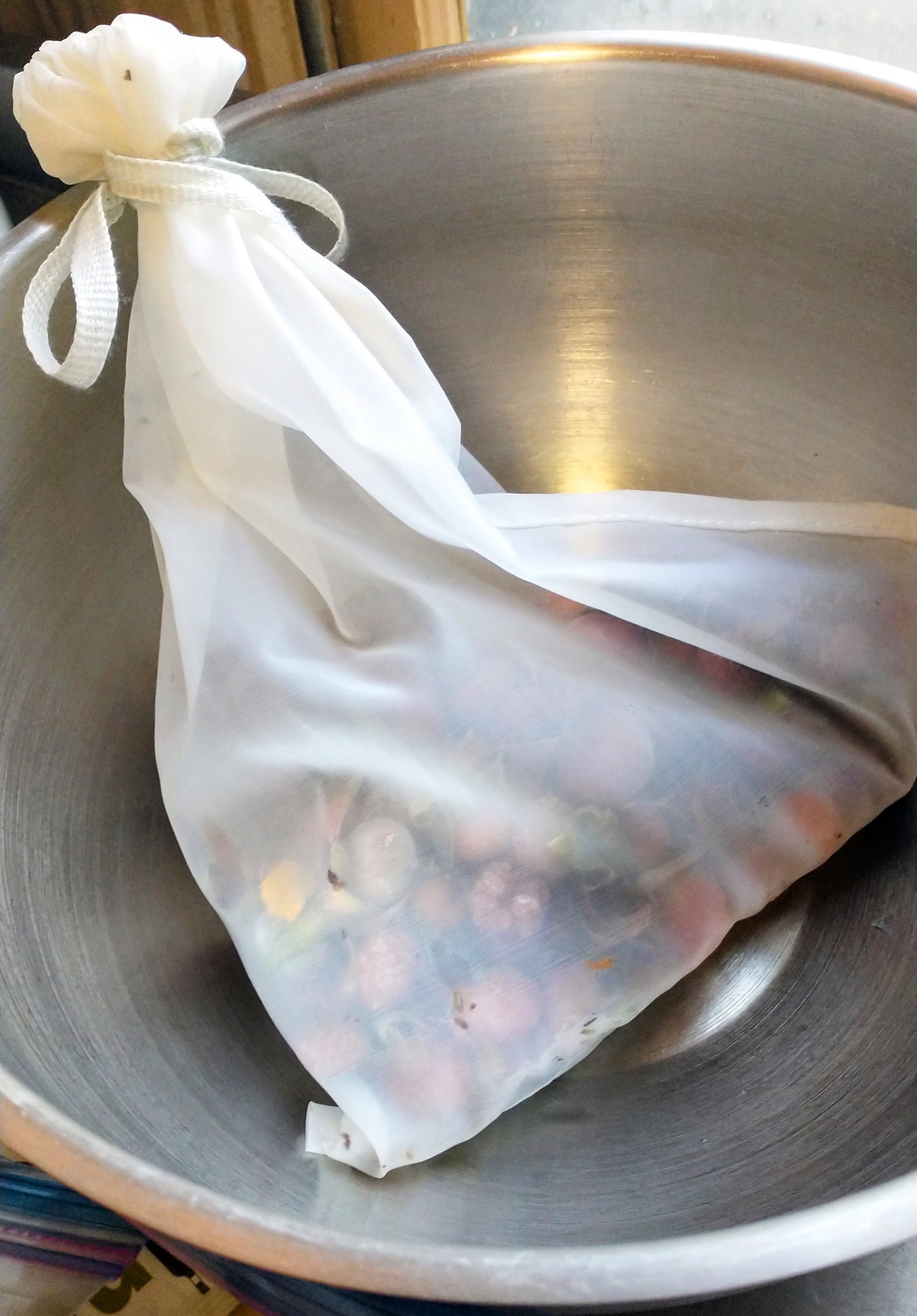 a nylon mesh bag filled with rose hips and other berries in a stainless steel bowl
