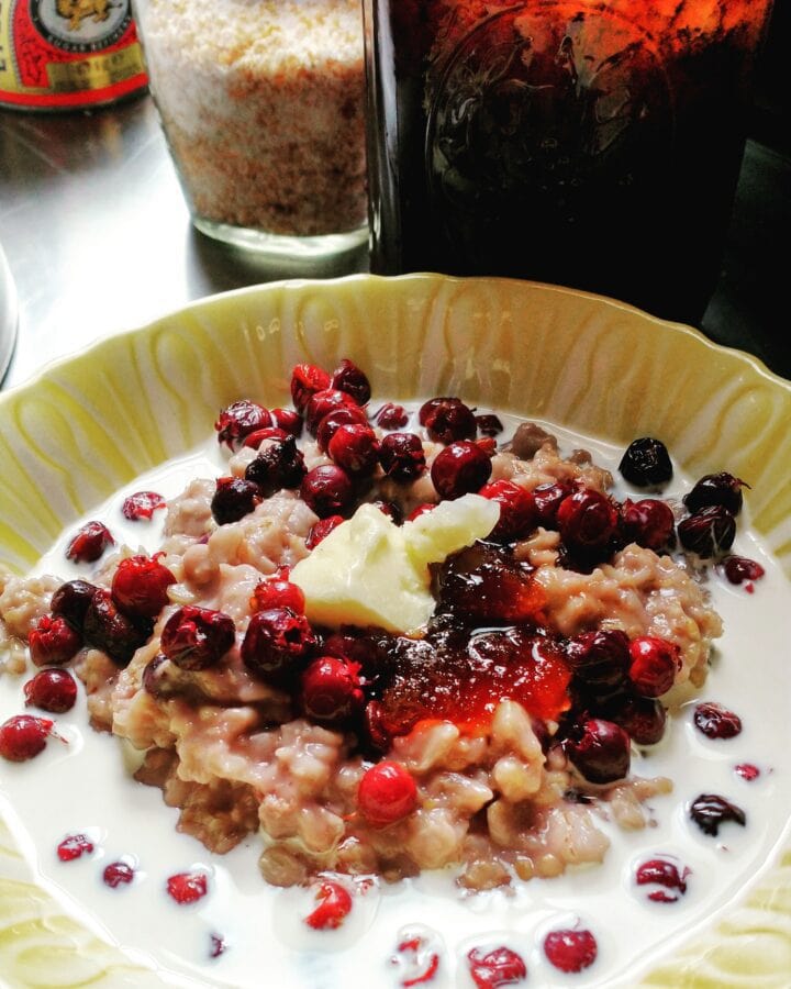 a bowl of oatmeal ringed with cream and dotted with brightly colored wild berries, golden yellow Irish butter, and berry blossom honey