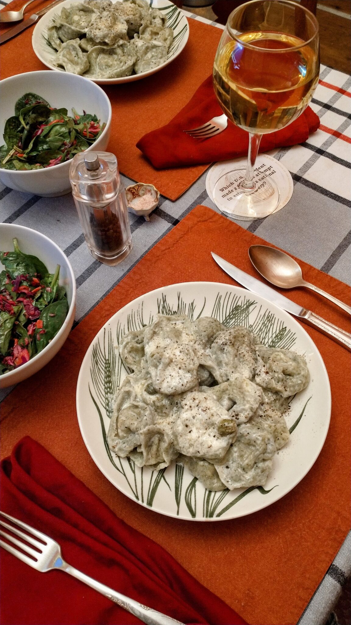 a table set with two bowls of tortellini in cream sauce, bowls of salad, silverware, and white wine