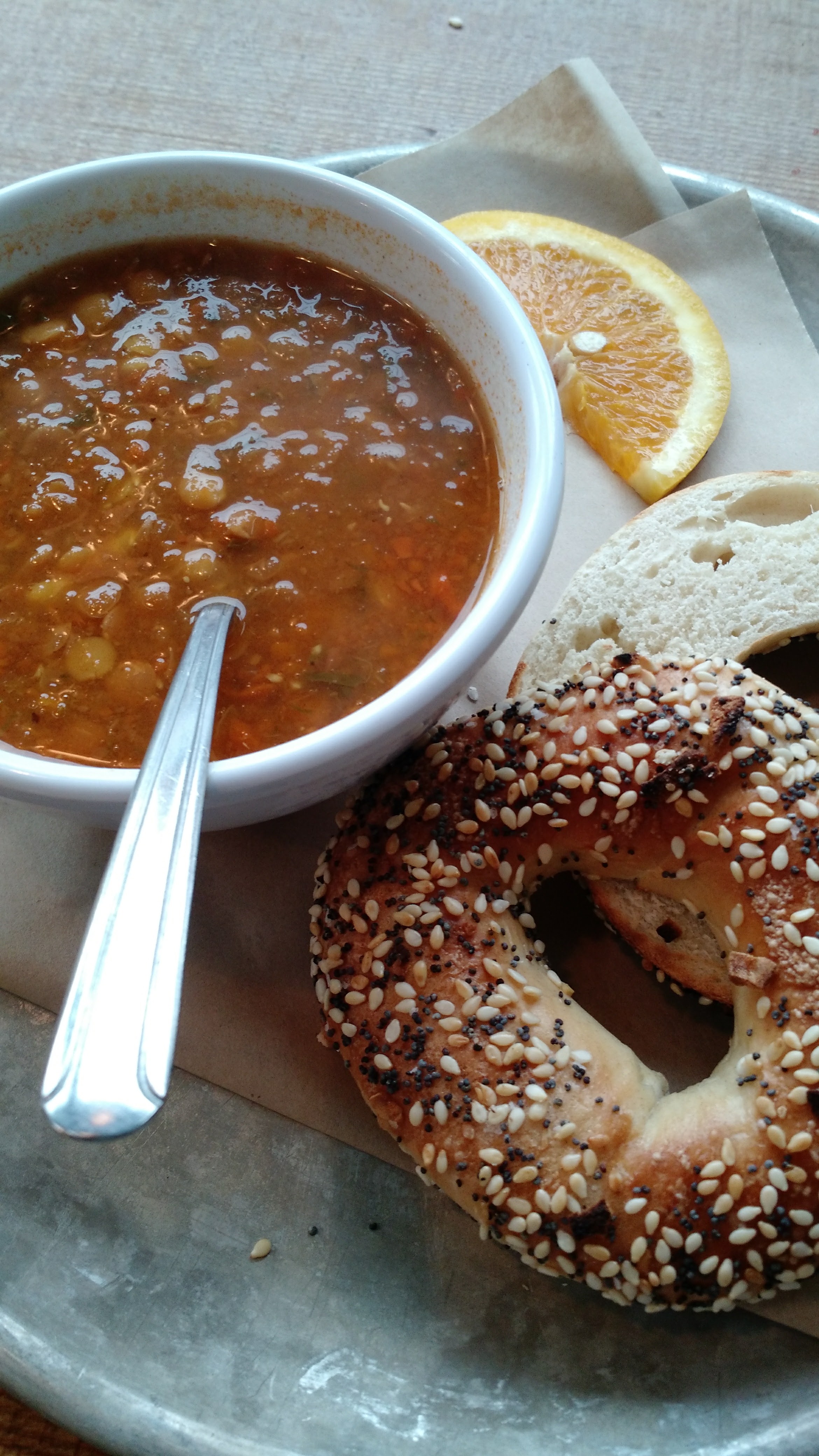 bowl of lentil soup, everything bagel, and a citrus slice
