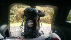 silhouette of a hiker readying his backpack in the back of a vehicle 
