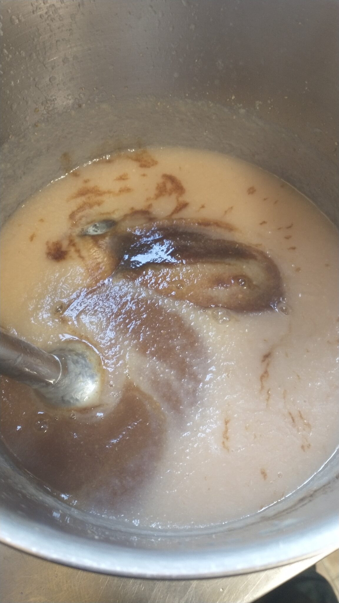 pear puree, brown sugar, and spices in a stockpot being mixed with an immersion blender.