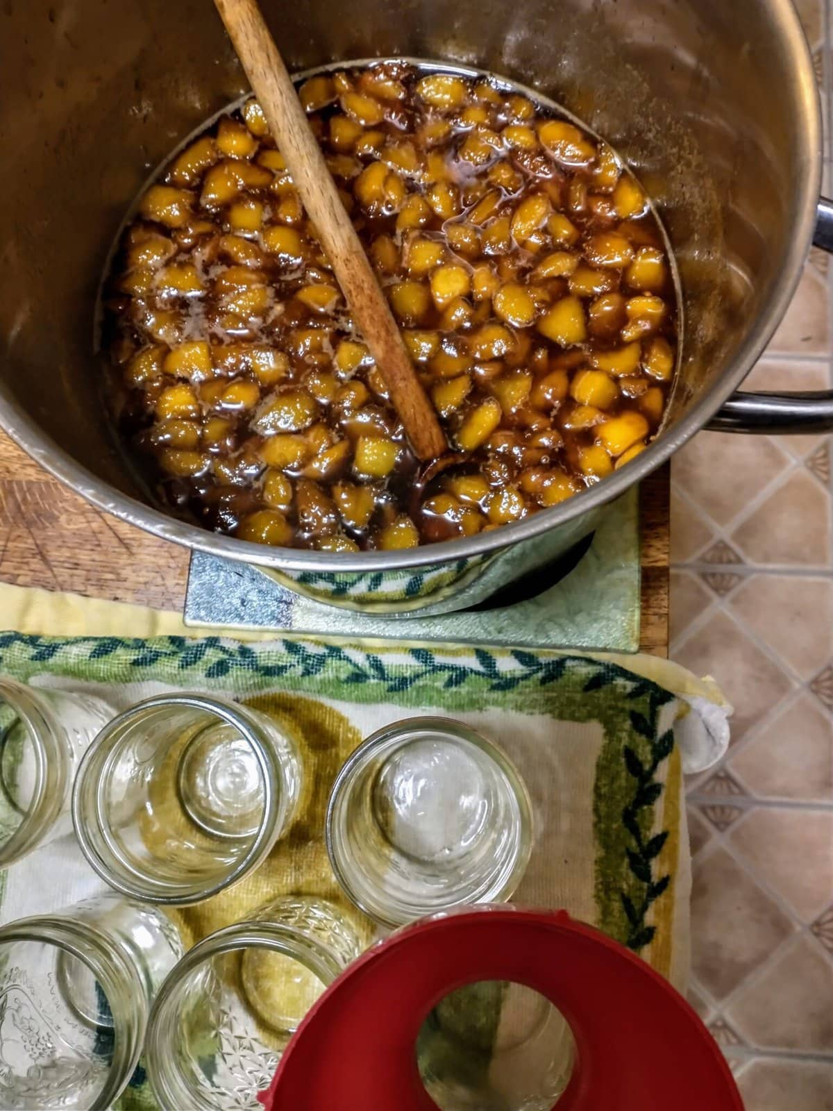 a pot of whiskey brown sugar peach compote in front of a tray of canning jars.