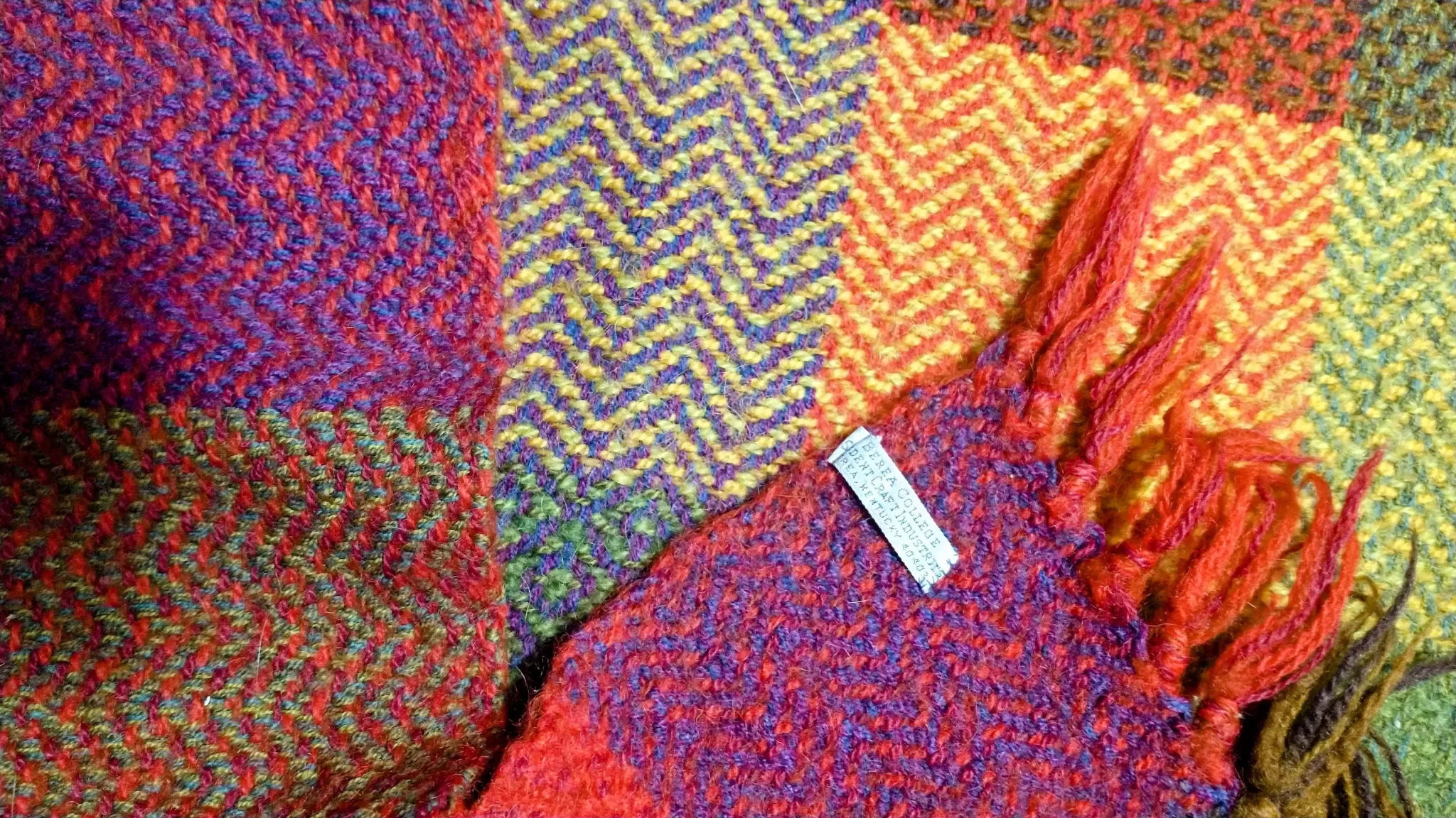 colorful handwoven blanket with herringbone pattern and a tag that reads, "Berea College Student Craft Institute, Berea Kentucky 40402"