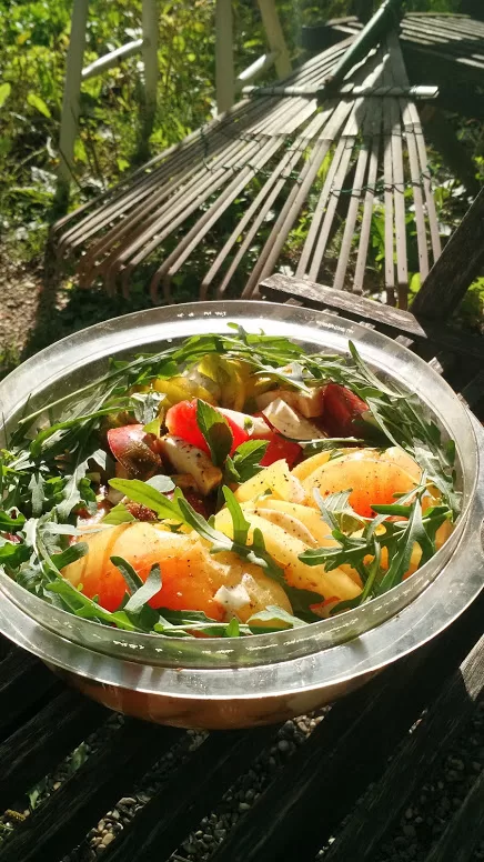 heirloom tomato caprese salad with homegrown arugula in a bowl in the garden. A bamboo rake and chair are in the background