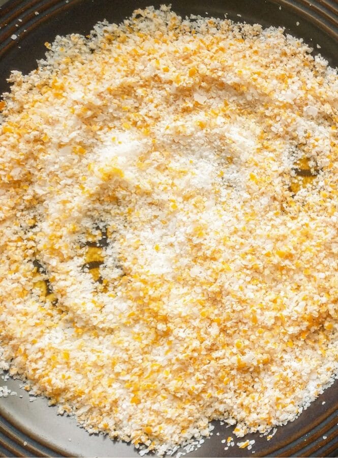 a dark brown plate covered with a thin layer of freshly made citrus salt spread out to dry. White salt flakes and citrus zest