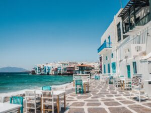 a beachside cafe on the aegean sea, with a stone patio and whitewashed stone buildings with colorful doors and windows