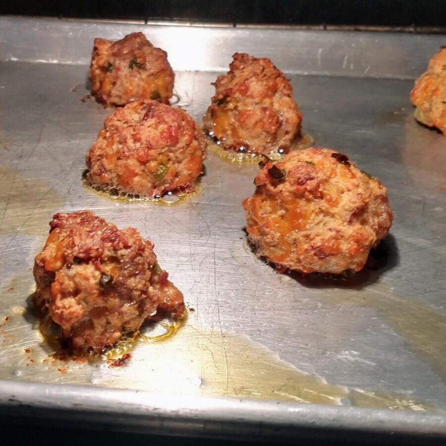 southern sausage and cheese balls on a sheet pan in the oven. they are fully baked and light golden brown.