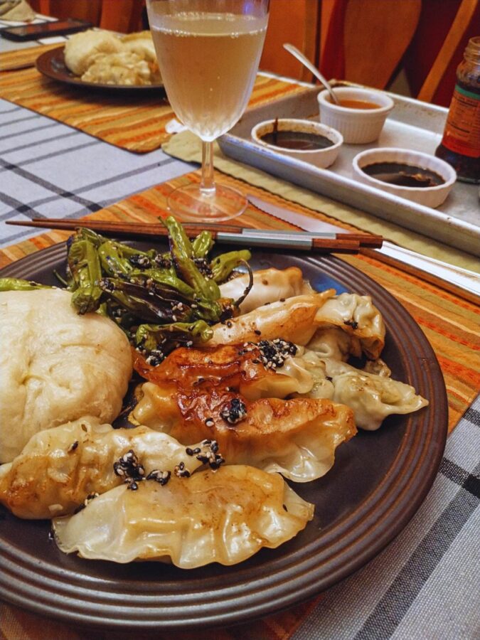 brown ceramic dinner plate with chopsticks, a steamed bun, potstickers, and shishito peppers with dipping sauces