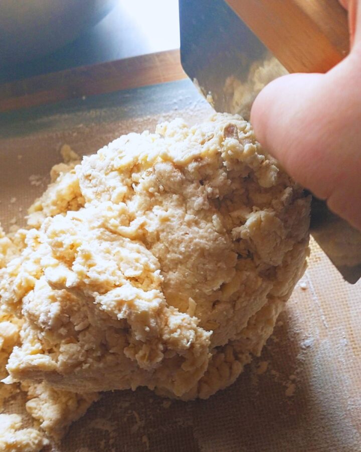 a shaggy dough being folded over on a silicone baking mat with a metal bench scraper.