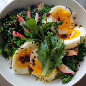 rice bowl with sauteed greens, halved jammy eggs, sliced radish, and black sesame seeds