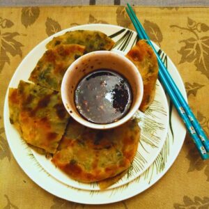 a plate with scallion pancakes, soy ginger dipping sauce, and chop-sticks