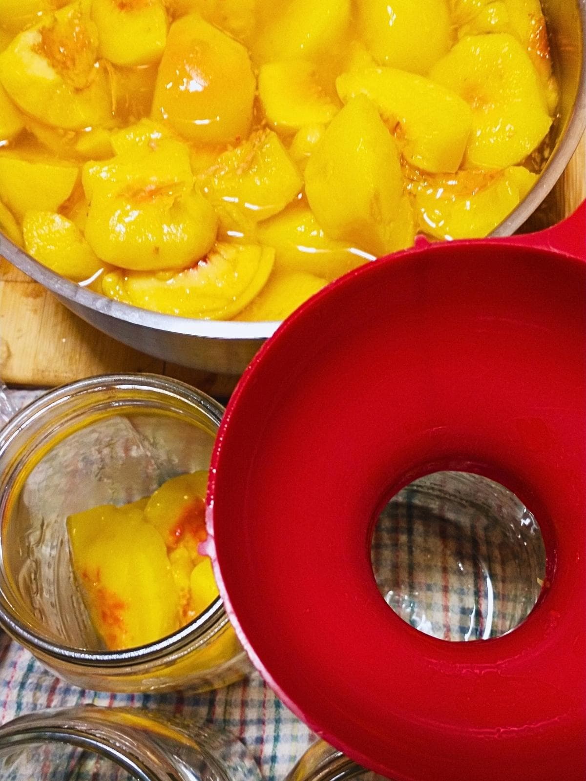 a bowl of summer peach slices being put into jars for canning using a canning funnel