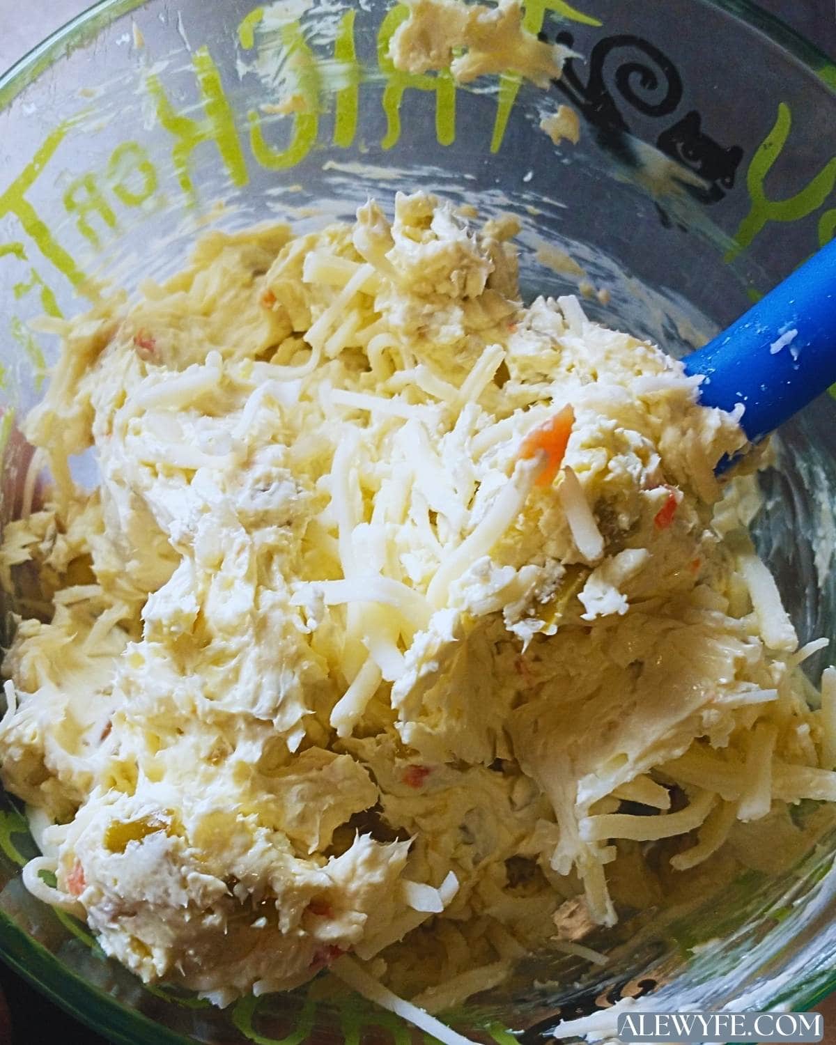 folding in grated cheese to spicy pizza spread with a spatula