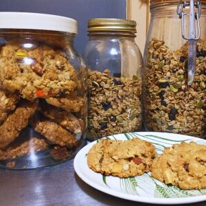 a plate with two peanut butter oatmeal trail mix cookies, with a jar of cookies and two jars of homemade granola in the background