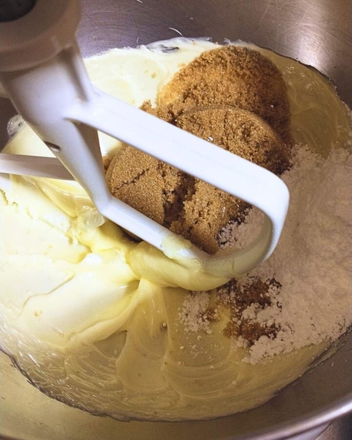 the bowl of a stand mixer with creamed butter and scoops of brown and powdered sugar.