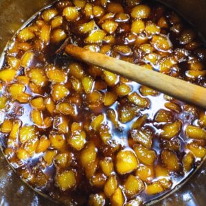 top view into a pot of whiskey peach brown sugar compote with a wooden spoon stirring the pot