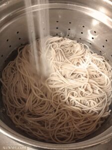 freshly cooked soba noodles being rinsed with cold water in a stainless colander to make cold soba noodles