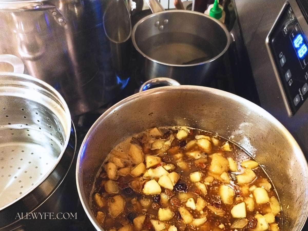 a pot of simmering spiced pear chutney on the stove, surrounded by other pots
