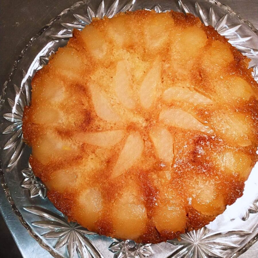top-view photo of a pear upside-down cake on a cut crystal platter, with pear sections arranged in a spiral pattern in the top of the cake