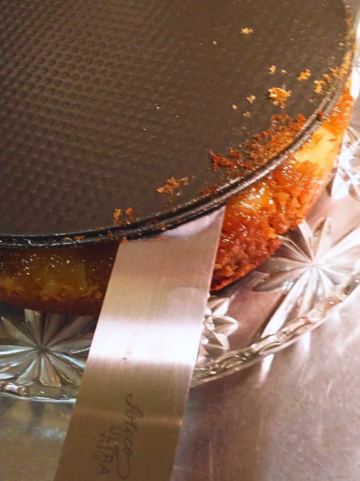 unmolding a coriander and brown sugar pear upside down cake onto a crystal platter using a long thin metal spatula