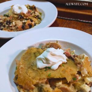 two white wide rimmed bowls with portions of green chile tamale pie casserole with a dollop of sour cream on top