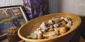 a bamboo oval tray with an array of small stones, crystals, trinkets, feathers, and acorns on a shelf, along with a framed postcard from the maxwell street market of a street vendor selling Howlin' Wolf records and a box made from an old LP of dance music with a forest motif