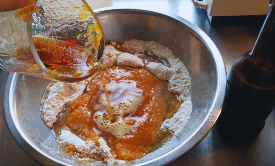 a mixing bowl filled with ingredients for vegan pumpkin cookies. The liquid ingredients are being poured into the center of the bowl