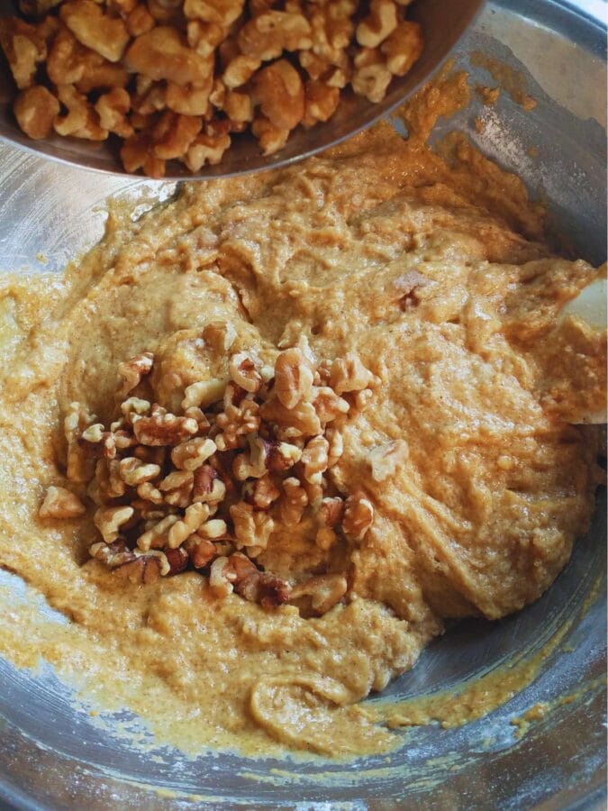 pouring chopped walnuts into the mixed vegan pumpkin cookie batter.
