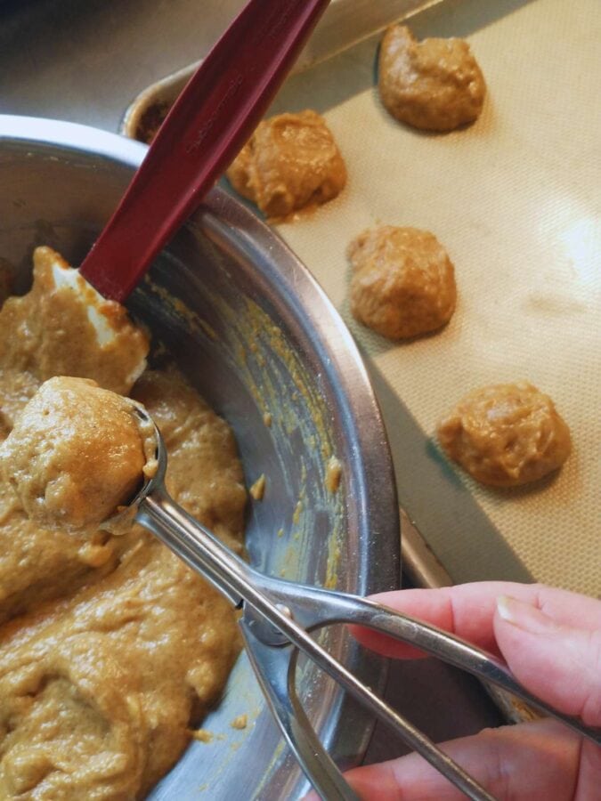 scooping batter for vegan pumpkin spice cookies onto cookie sheets lined with silicone nonstick sheets.
