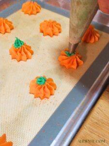 piping pumpkin shaped spritz cookies onto a cookie sheet lined with silicone baking mat