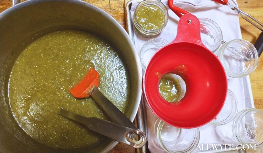 a pot of roasted salsa verde being ladled into clean canning jars with a bright red canning funnel