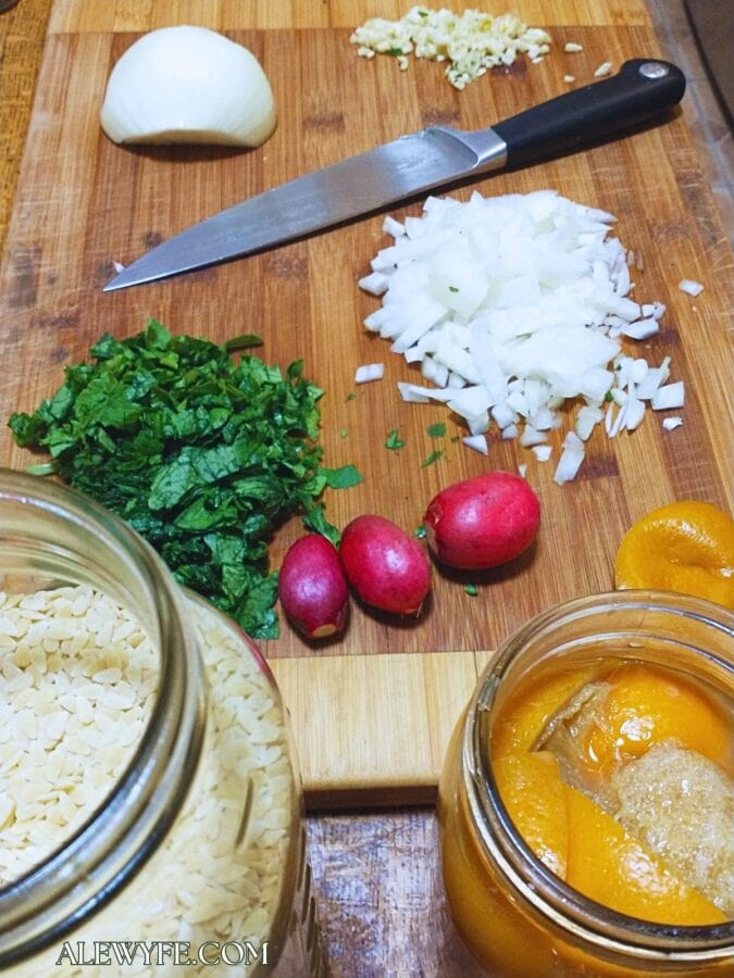 mise en place for white bean orzo, showing ingredients prepped on a cutting board next to a jar of dry orzo pasta and a jar of preserved meyer lemons.