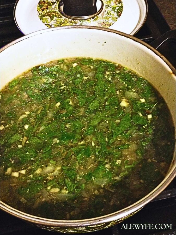A pot of white bean orzo cooking, with bright greens floating on top of the broth that hasn't yet been absorbed into the orzo.