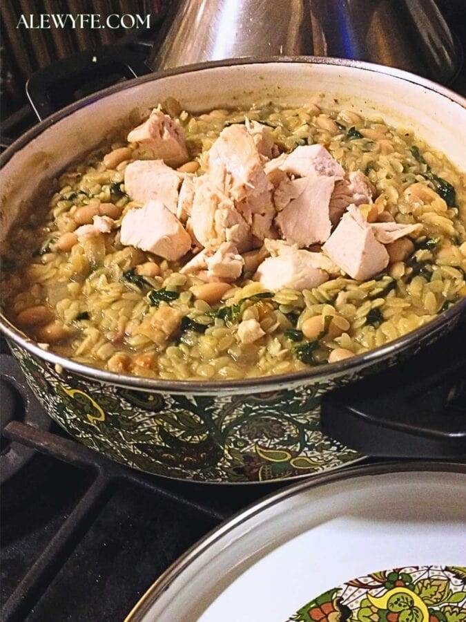 diced chicken being folded into a pot of white bean orzo.