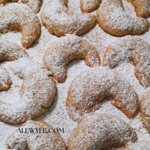 a tray of freshly baked yule moon crescent cookies, dusted with powdered sugar
