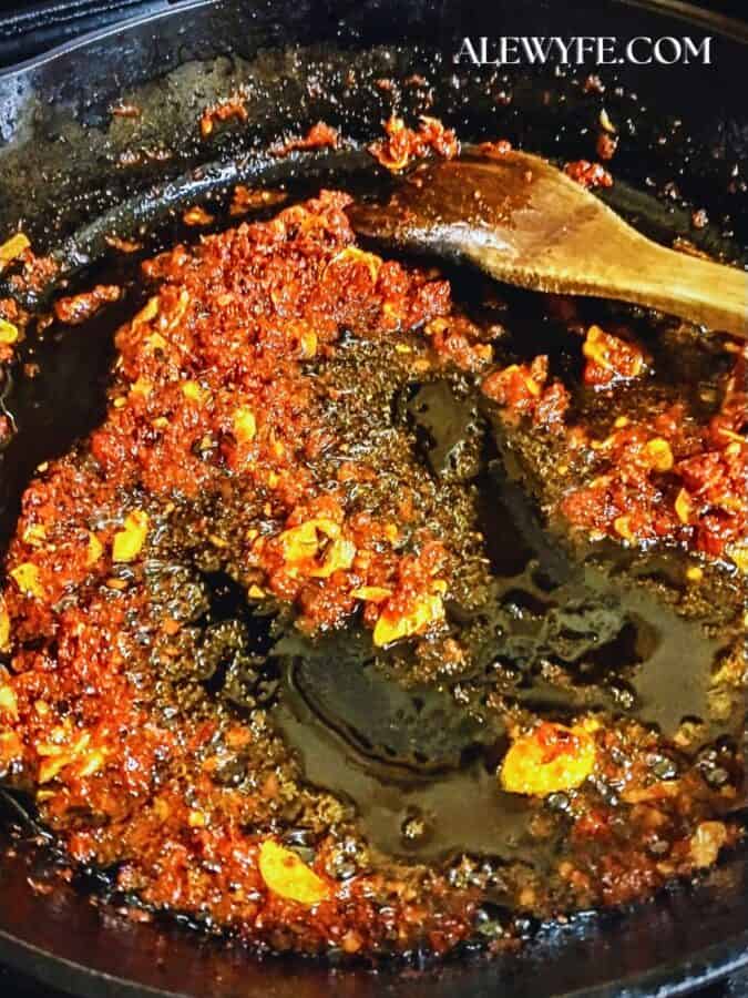 sliced garlic, red chili flakes, and a bit of tomato sauteing in olive oil in a black iron pan, being stirred with a wooden spatula