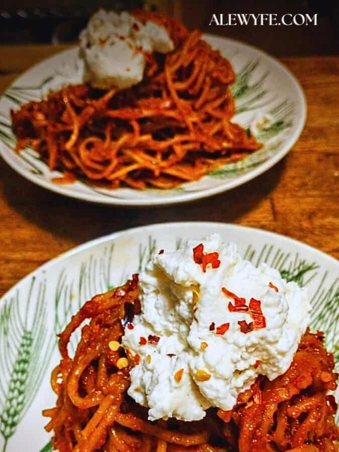 two bowls of assassin's spaghetti topped with fresh mozzarella crema and red chili flakes
